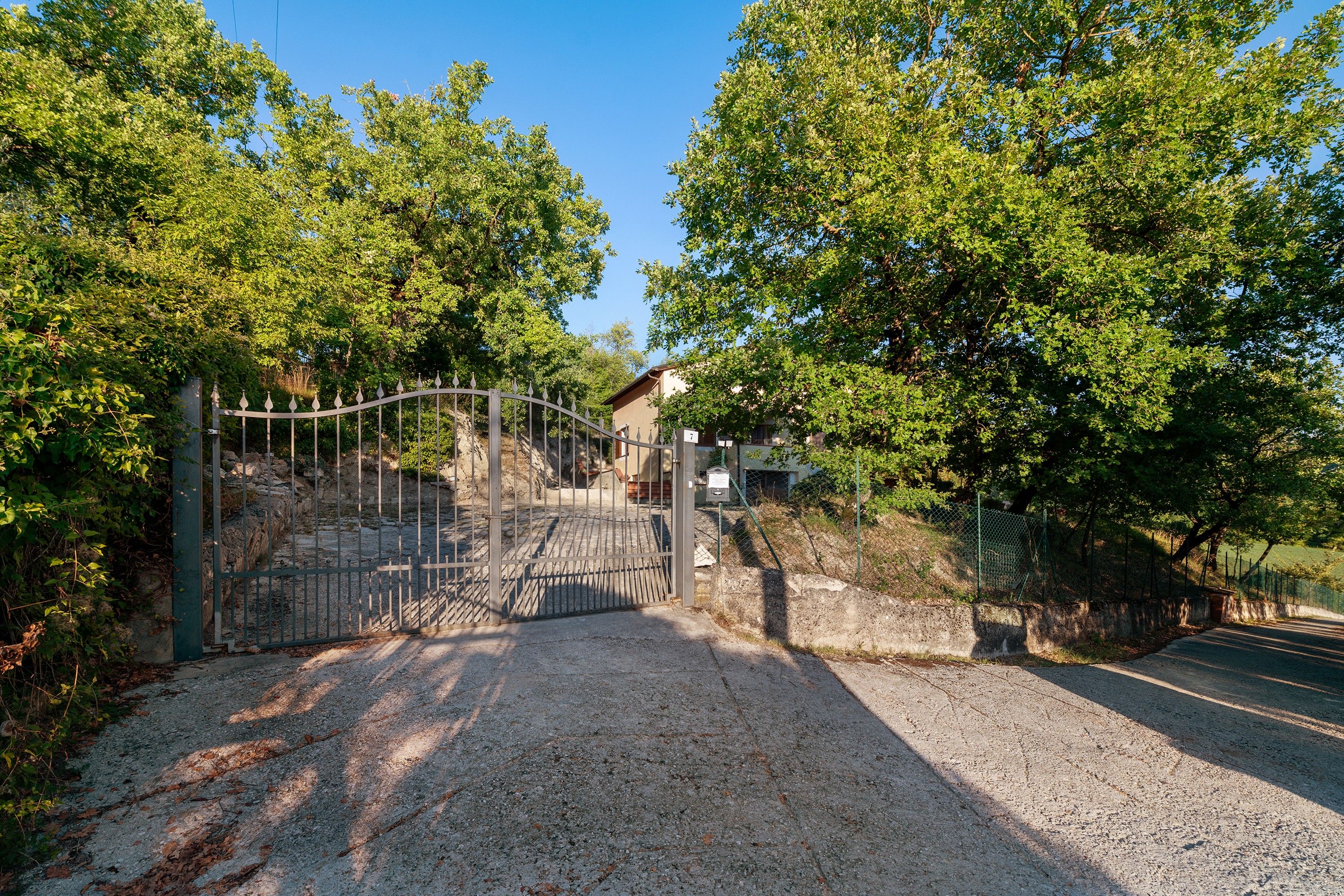 A gated entrance with a gravel path leading to a building, surrounded by trees.