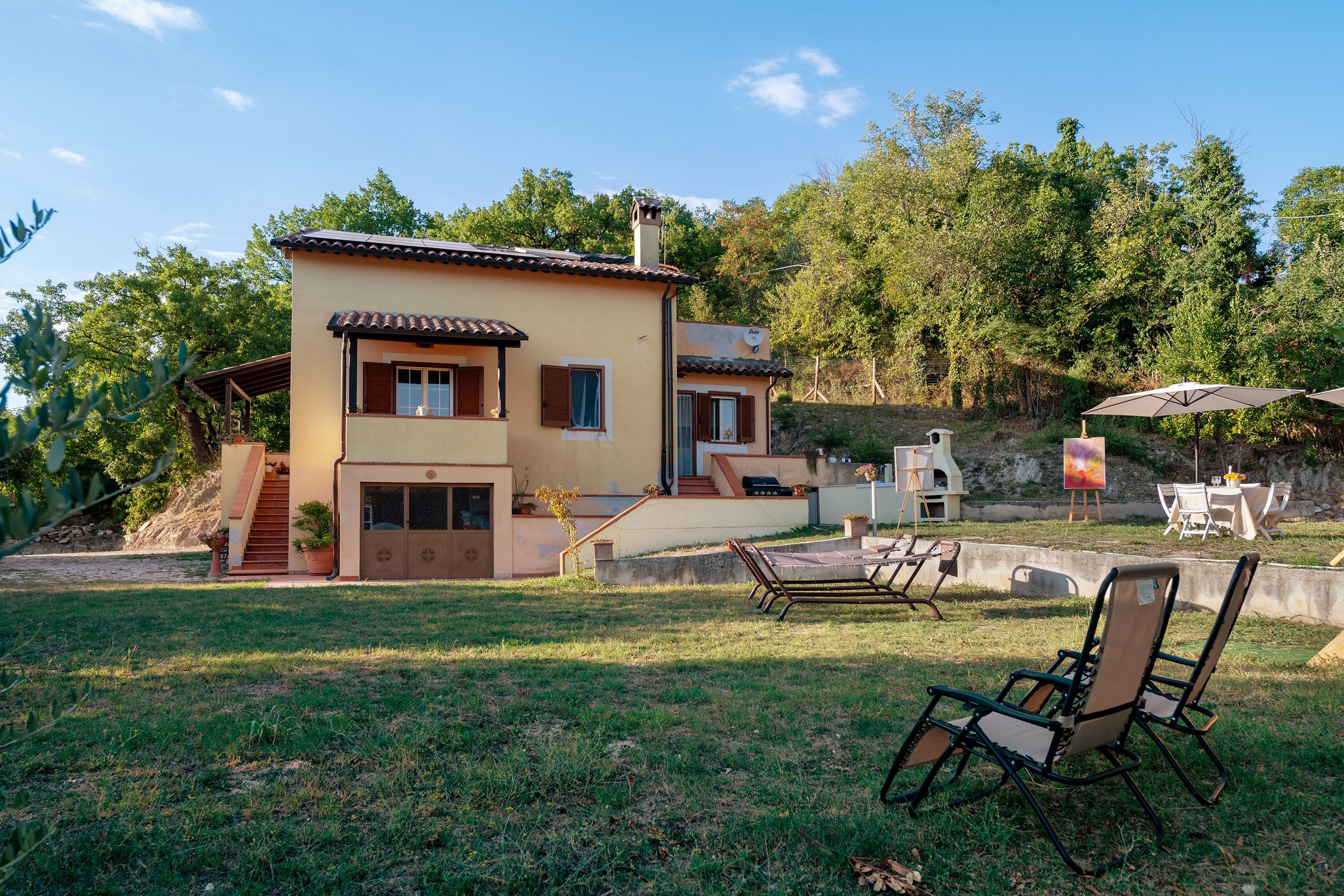Une maison à deux étages dotée d’un patio, d’un espace salon extérieur et offrant une vue sur les arbres environnants.