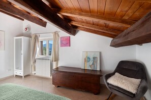 Una habitación con techo inclinado, un aparador de madera, una silla con almohada mullida, un radiador y una puerta que da al exterior.