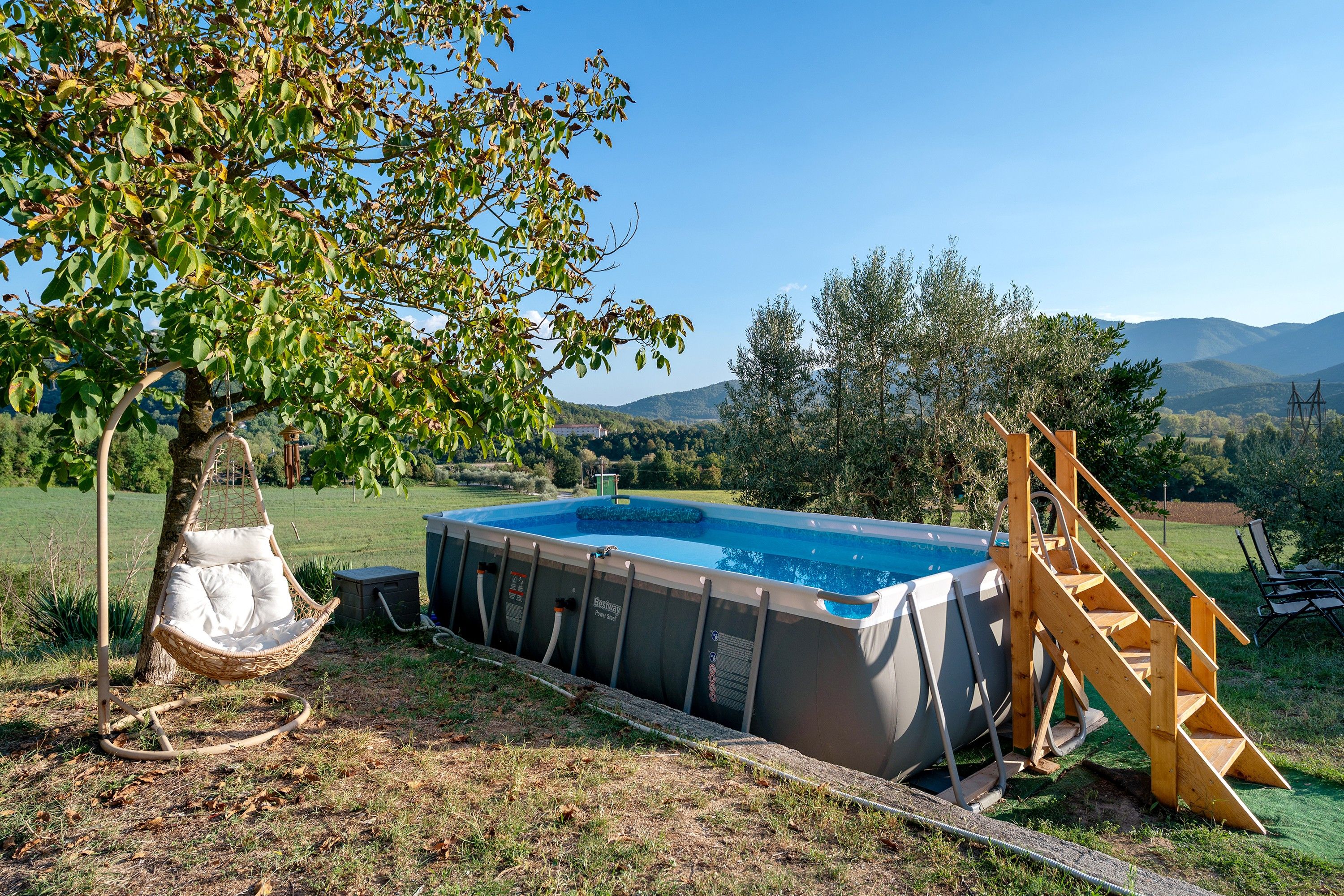 Un jardin avec une piscine, une échelle en bois et un fauteuil suspendu.