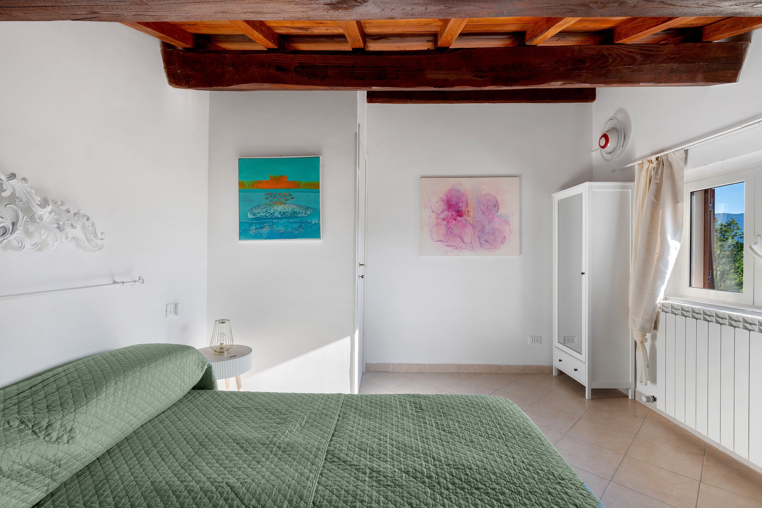 Un dormitorio con una cama, un armario, un radiador y dos cuadros en la pared.