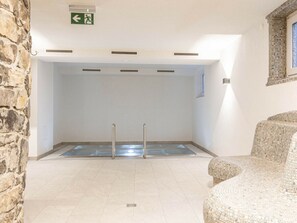 Una habitación con piscina, pared de piedra y un letrero de salida verde.