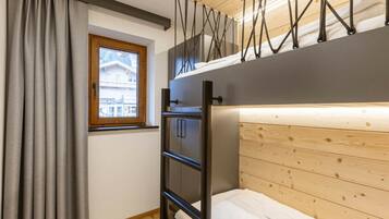 A compact room with a bunk bed, a window with curtains, a wooden ceiling, and a metal ladder.