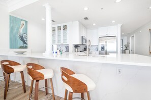 Una cocina moderna con armarios blancos, encimera de mármol y taburetes de madera.