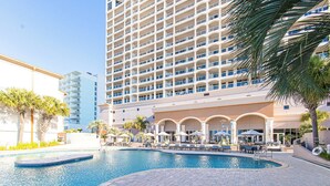 A hotel with a swimming pool, a multi-story building, and palm trees. - Updated Luxury Gulf-Front 3BR | Beach Club 1404, Pools, Spa & Beach Chairs (Pensacola Beach)