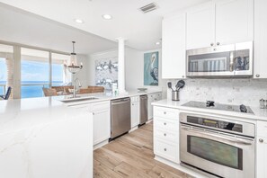 A modern kitchen with white cabinetry, a built-in oven, and a view to the outside. - Updated Luxury Gulf-Front 3BR | Beach Club 1404, Pools, Spa & Beach Chairs (Pensacola Beach)