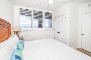 A bedroom with a bed, a nightstand, a lamp, a window with blinds, and a ceiling fan. - Updated Luxury Gulf-Front 3BR | Beach Club 1404, Pools, Spa & Beach Chairs (Pensacola Beach)