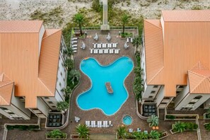 Eine Vogelperspektive eines Hotels mit einem zentralen Schwimmbad, mehreren Lounge-Bereichen und einer Strandlage.
