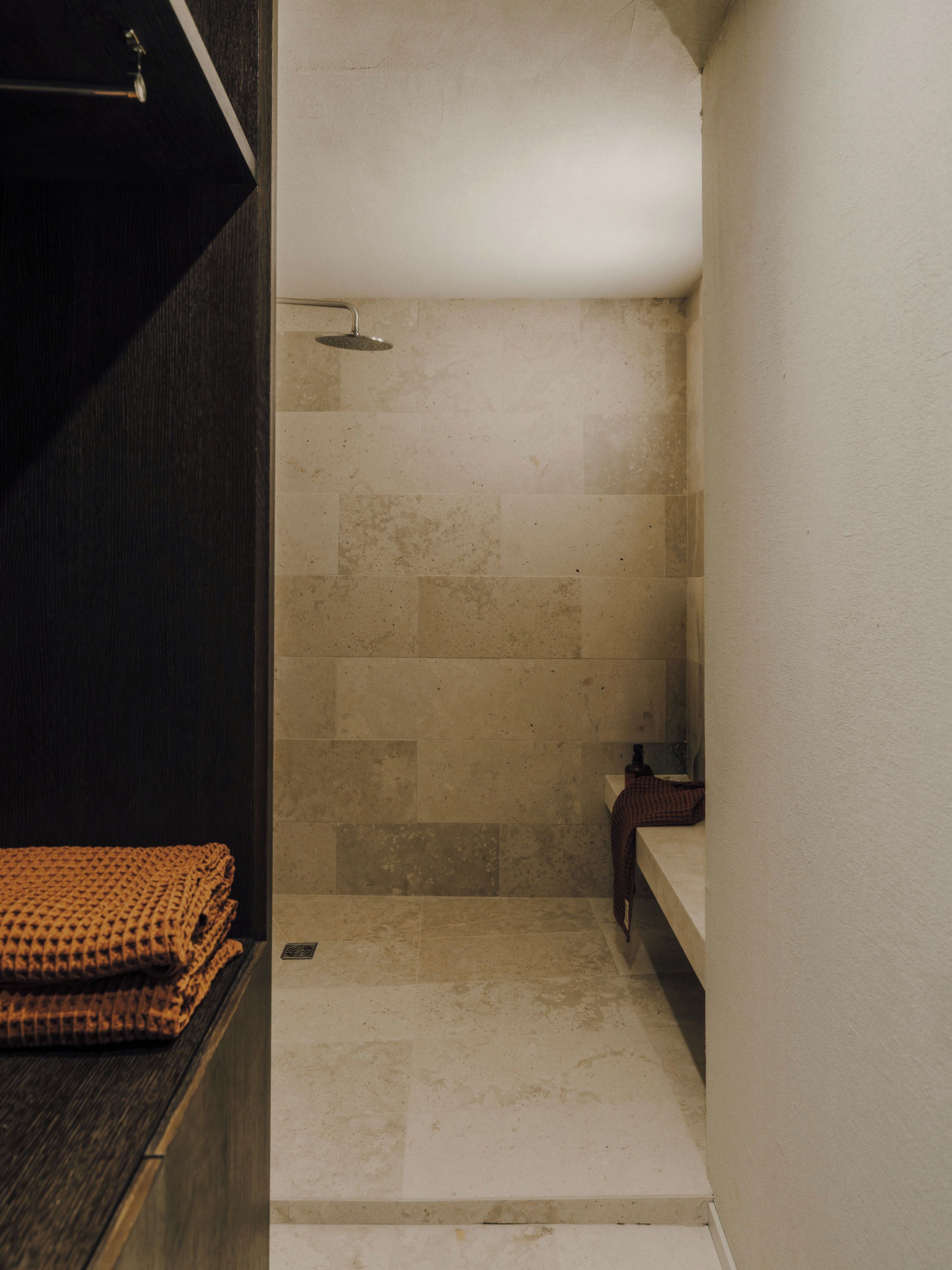 A narrow shower area with tiled walls and a dark wooden bench.