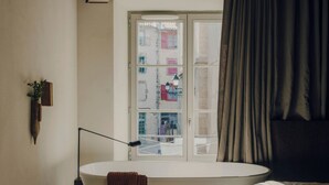 Un baño con bañera, una ventana con cortinas, una lámpara de pie y una toalla colgada en la pared.