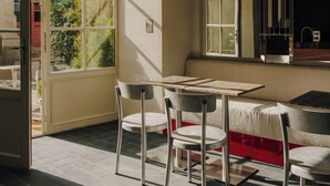 Un comedor con mesa y sillas, un ventanal con vistas a zonas verdes, y una cocina con lavaplatos y armarios.