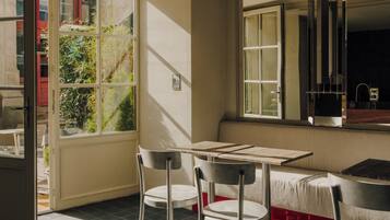 A dining area with a table and chairs, a window with a view of greenery, and a kitchen area with a sink and cabinets.