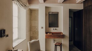 Un dormitorio con techo de madera, una cama grande, una ventana con cortinas, un armario de madera y un baño con espejo y lavabo.