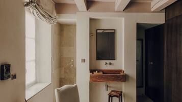 A bedroom with a wooden ceiling, a large bed, a window with curtains, a wooden cabinet, and a bathroom with a mirror and sink.