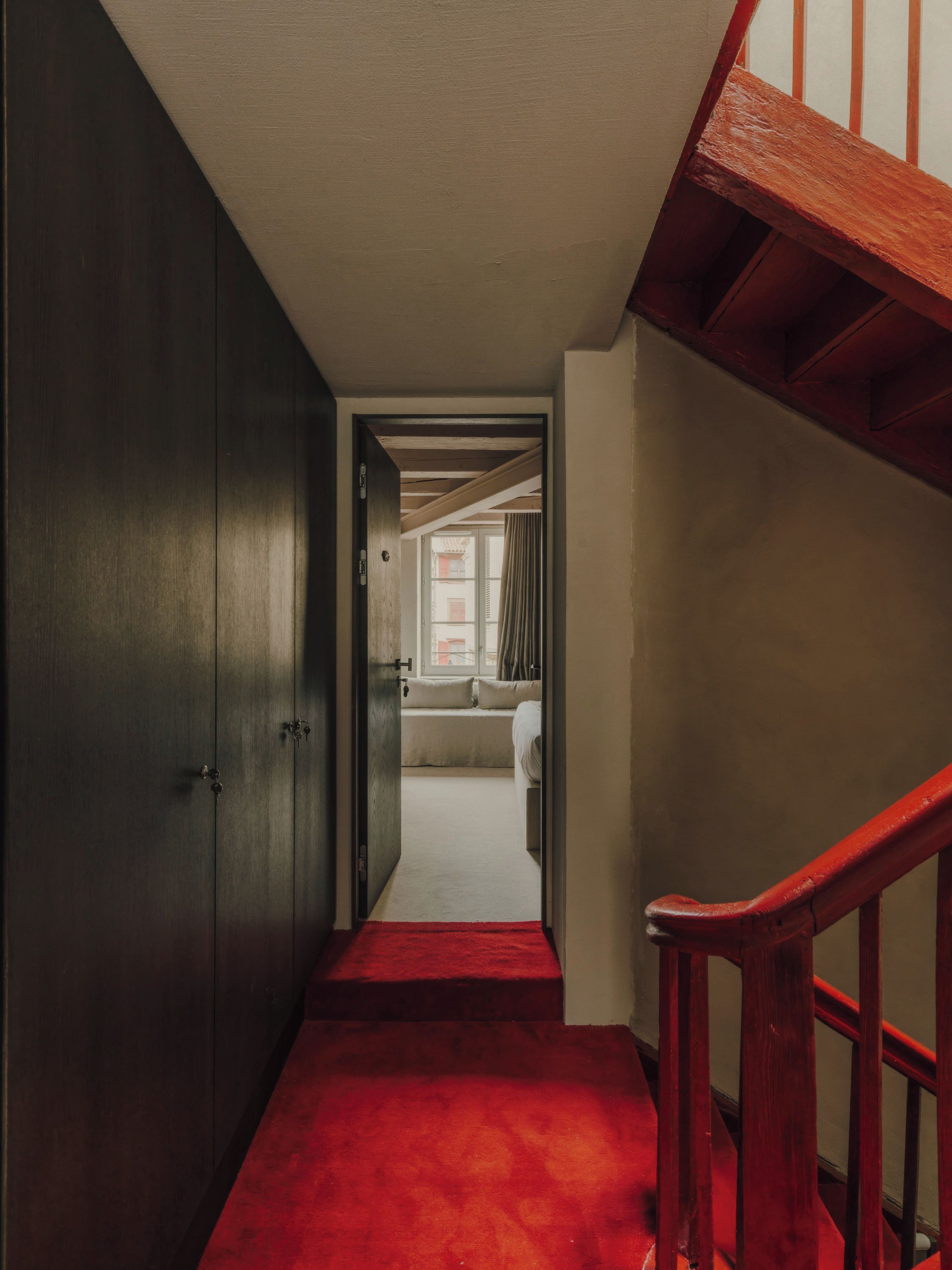 Un couloir menant à une chambre avec une moquette rouge, un escalier en bois et une armoire.