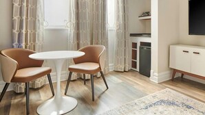 Een moderne eetruimte met een ronde tafel en twee stoelen, een keuken met een vaatwasser, en een televisie aan de wand.