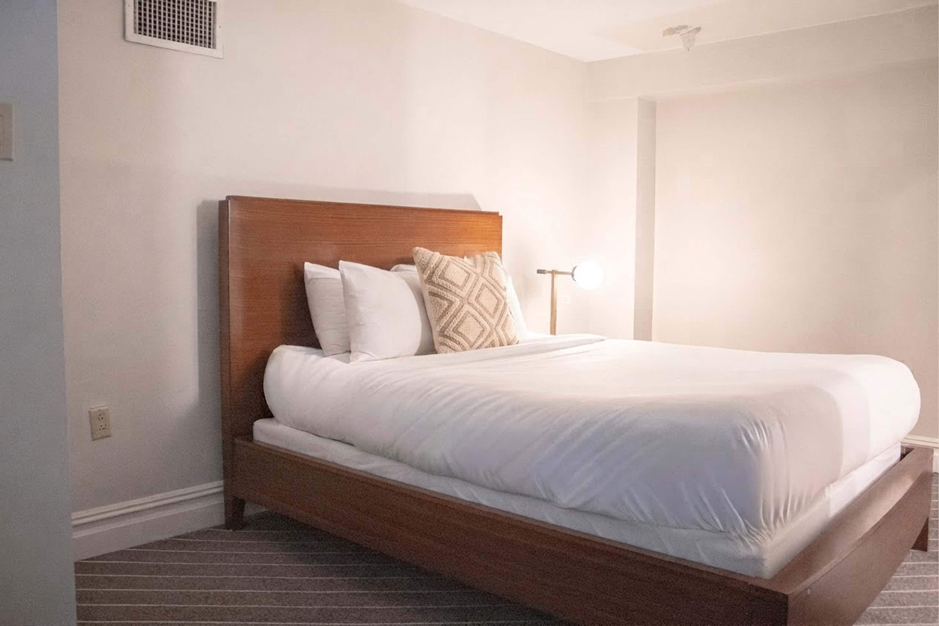 Un lit simple avec une tête de lit en bois, une literie blanche et un coussin décoratif à motifs.
