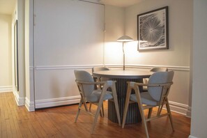 Ein Essbereich mit einem runden Tisch, vier Stühlen, einer Stehlampe und einem gerahmten Kunstwerk an der Wand.