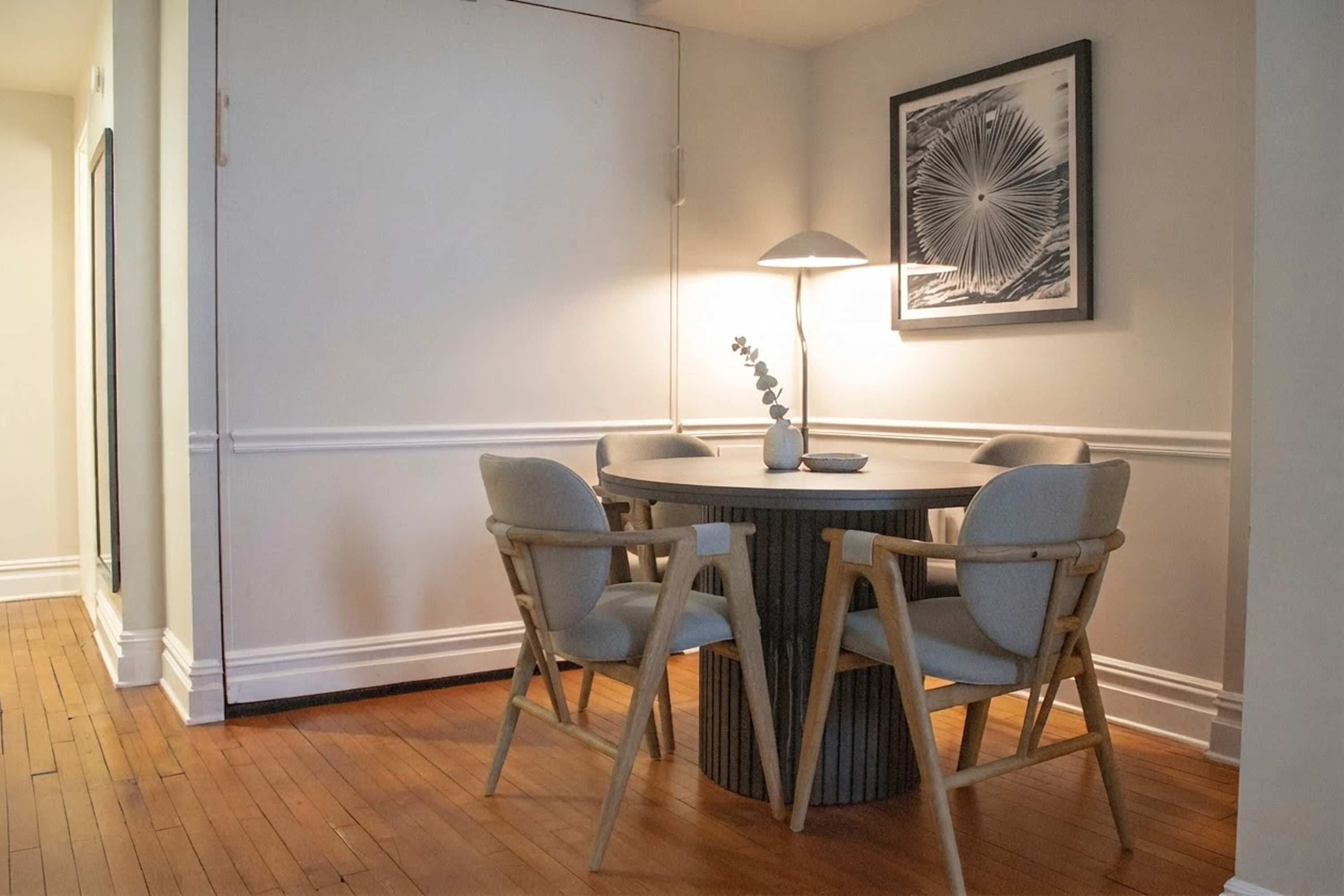 Un coin repas comprenant une table ronde, quatre chaises, un lampadaire et une œuvre d’art encadrée accrochée au mur.