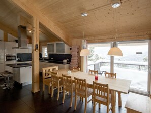A wooden interior with a dining table, chairs, a kitchen area, and a view through a large window. - Cabin in Turrach With Sauna and Balcony (Stadl-Predlitz)