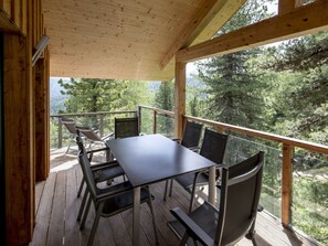 A wooden deck with a table and chairs, overlooking a forested area. - Cabin in Turrach With Sauna and Balcony (Stadl-Predlitz)