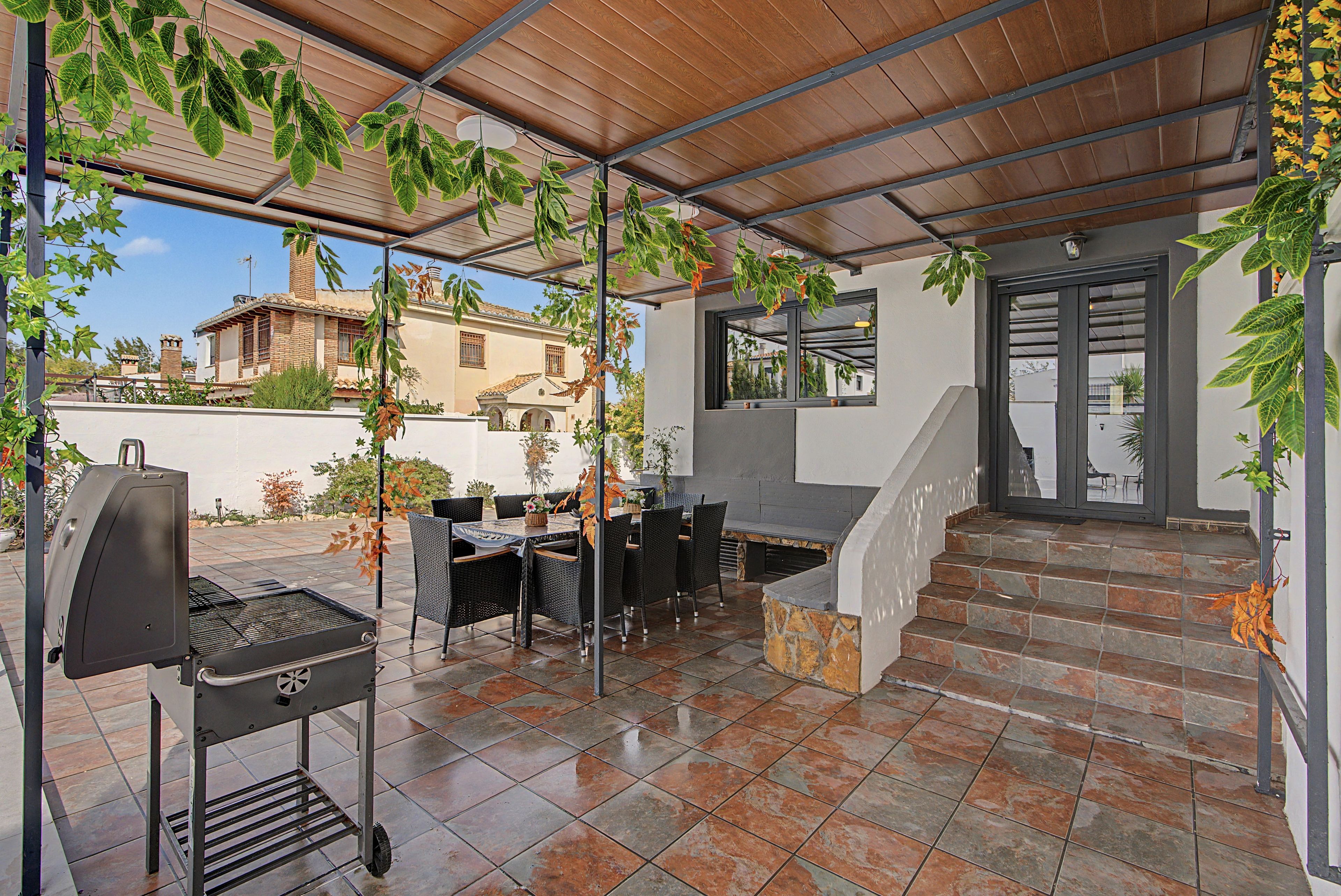 Une terrasse extérieure équipée d’un barbecue, d’une table à manger, de chaises et d’un escalier menant à un niveau supérieur.