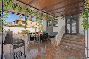 An outdoor patio with a grill, dining table, chairs, and a staircase leading to an upper level.