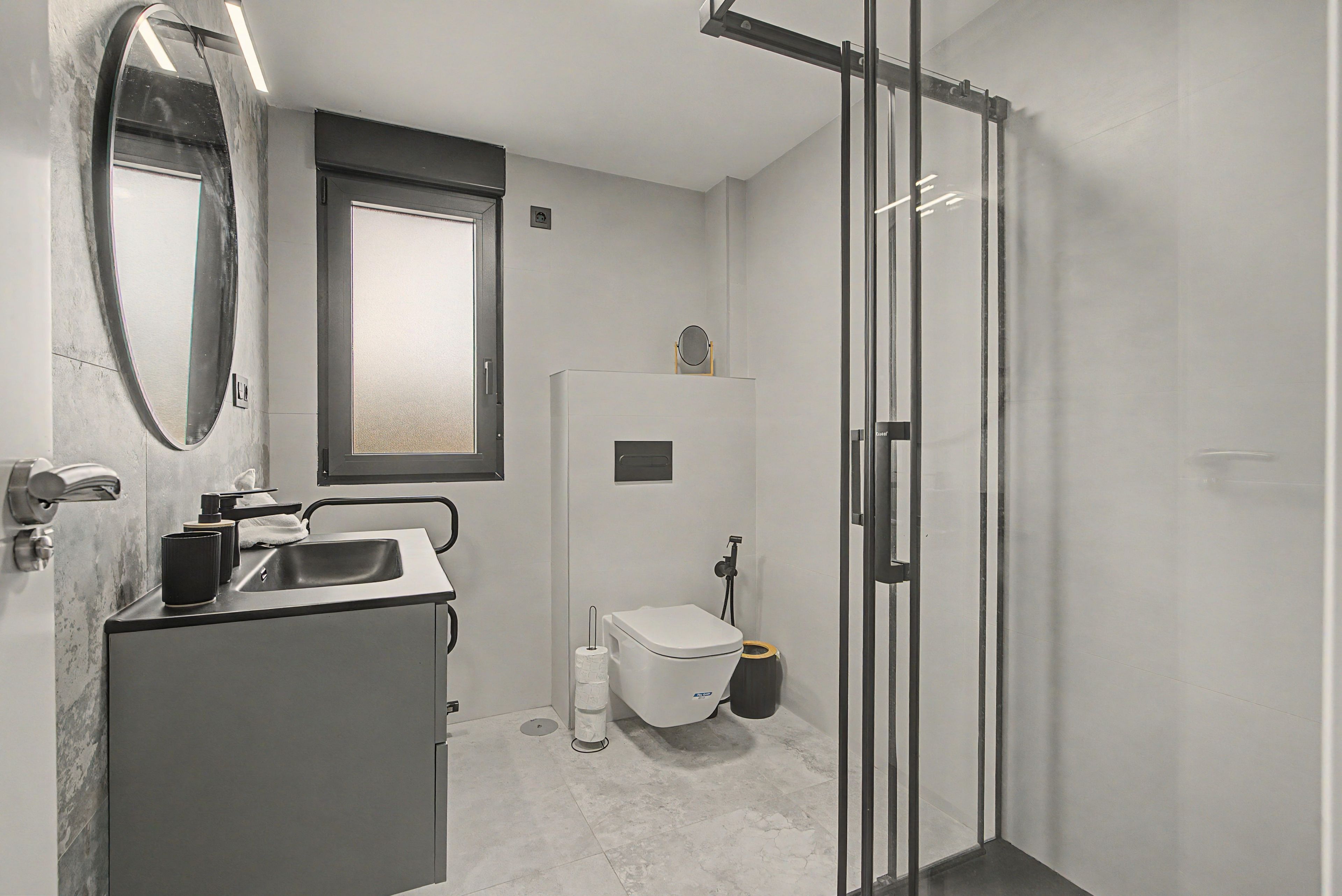 Ein modernes Badezimmer mit Duschkabine aus Glas, Toilette und Waschbecken mit Spiegel darüber.