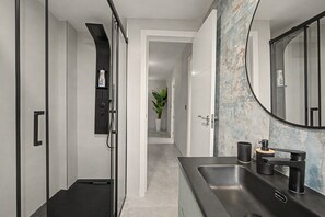 Une salle de bain moderne avec un lavabo noir, un grand miroir et une douche dotée d’un panneau de commande.