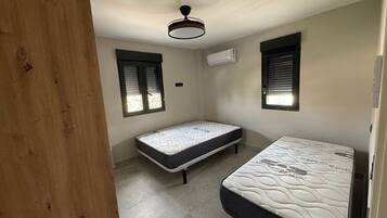 A room with two beds, a ceiling fan, and two windows with blinds.