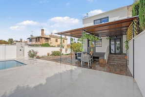 A modern outdoor patio with a pool, a barbecue area, and a covered seating space.