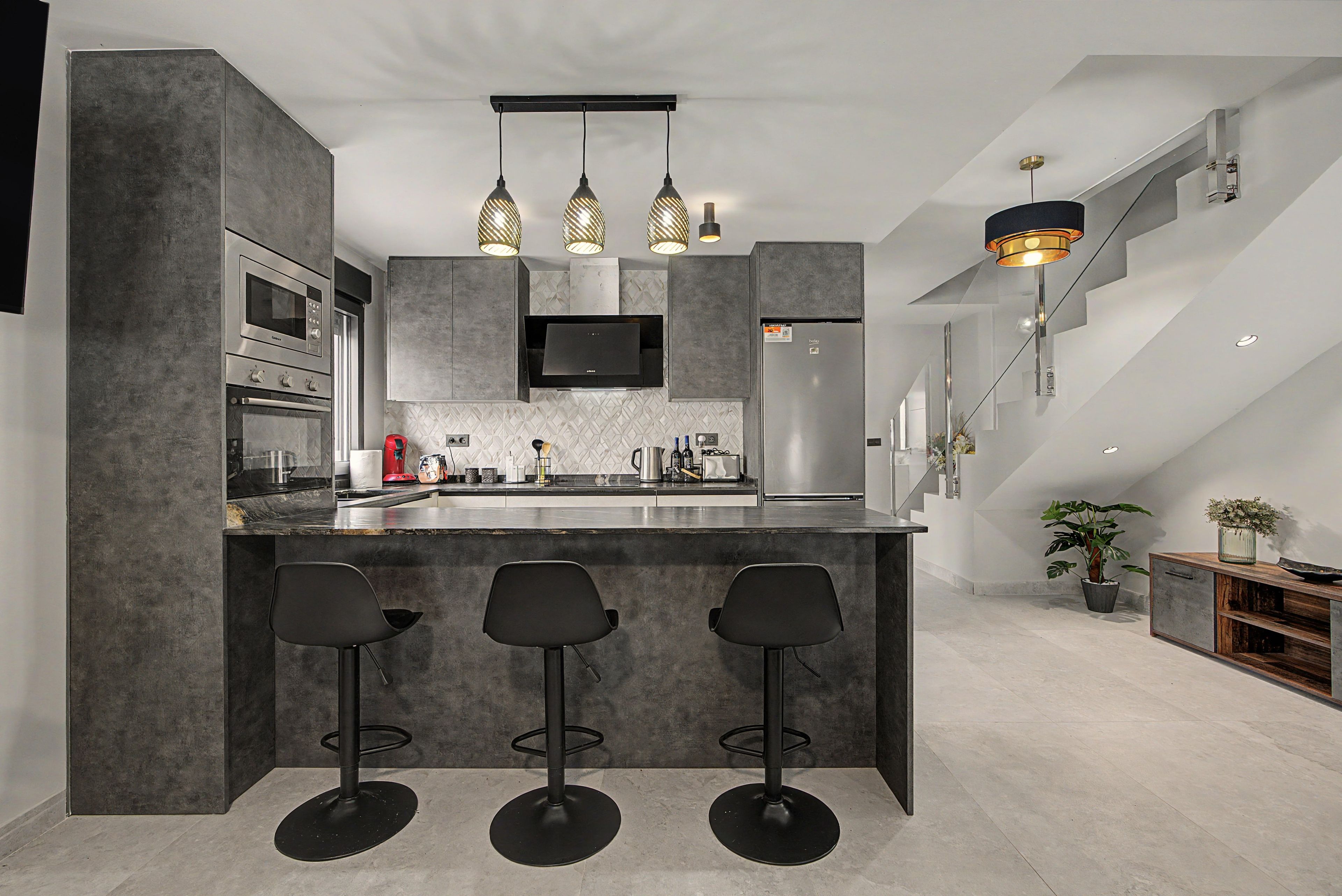 A modern kitchen with a central island, bar stools, and a dining area with a staircase.