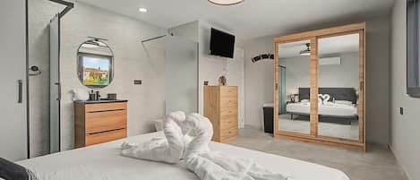 Un dormitorio moderno con cama, cómoda de madera, espejo, televisor y armario.