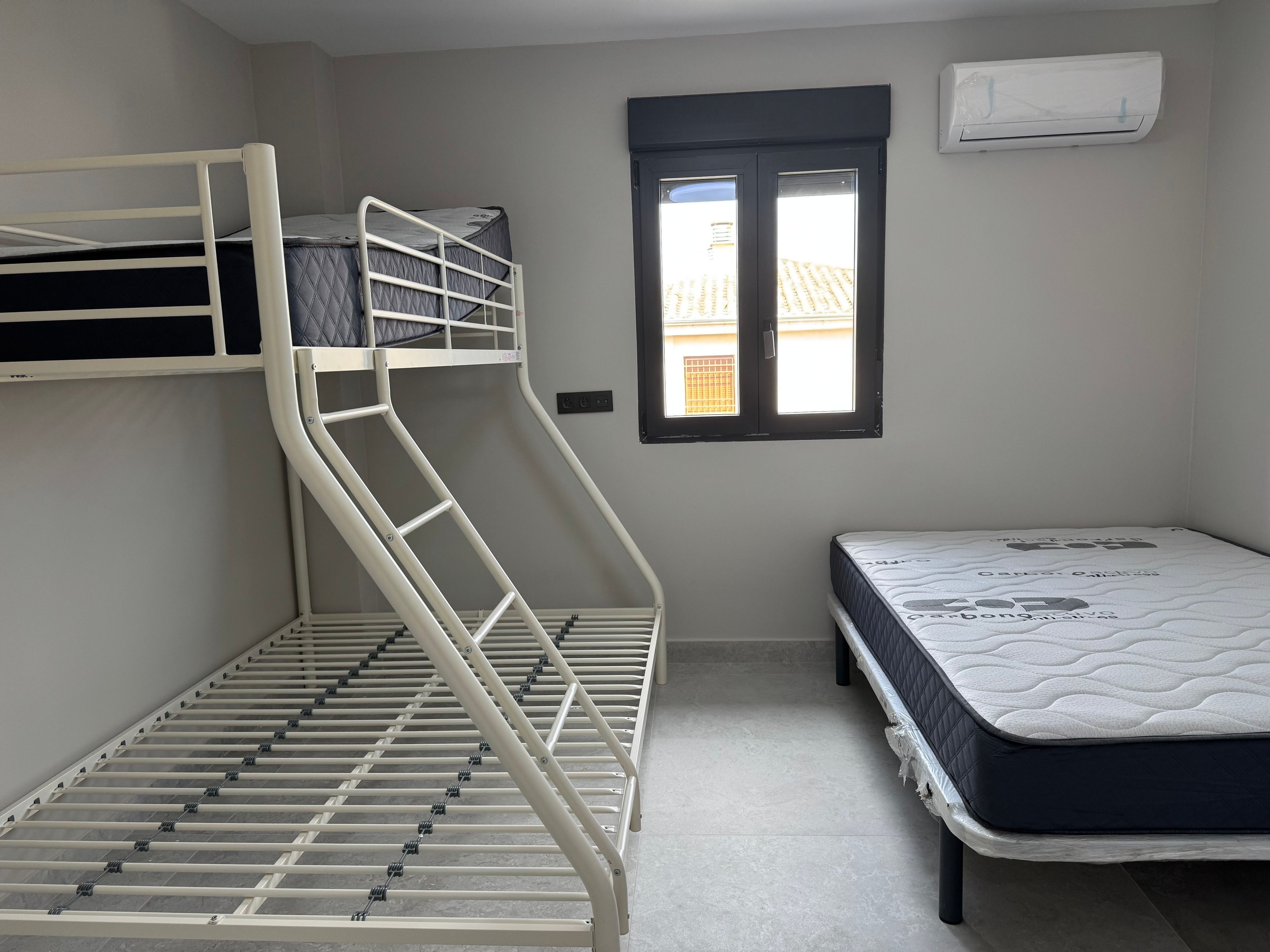 A room with bunk beds, a window, and an air conditioning unit.