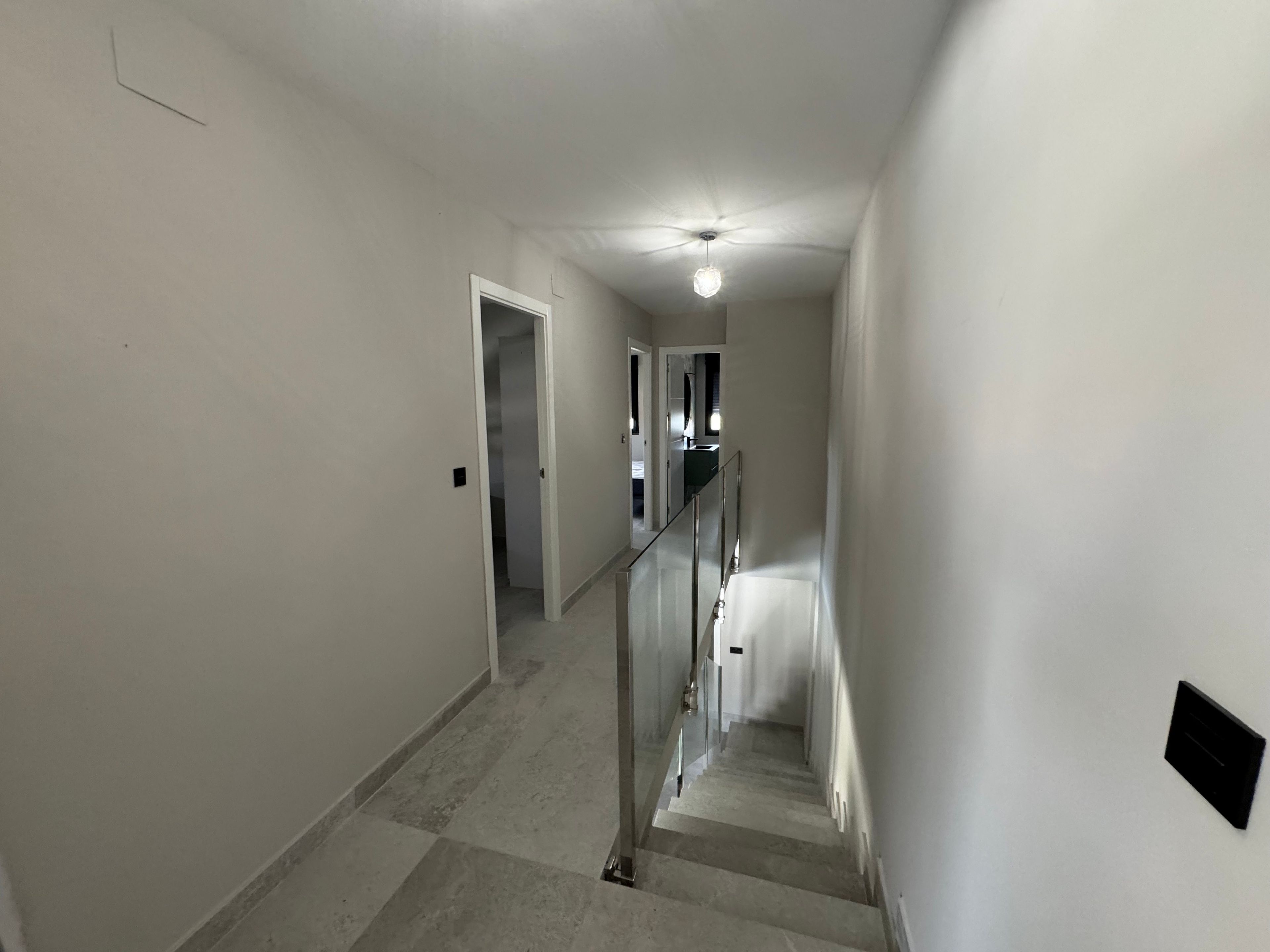 A narrow hallway with a staircase leading to another floor, a ceiling fan, and a light fixture.