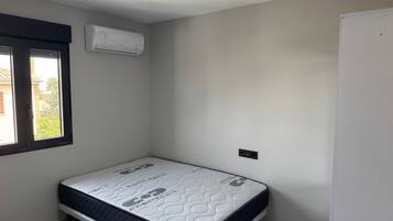 A small, clean room with a single bed, a window, and an air conditioning unit.