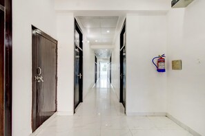 A corridor with doors on both sides, a fire extinguisher mounted on the wall, and a clean, tiled floor.