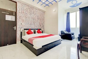 Una habitación de hotel con cama, escritorio, silla y ventana con cortinas.