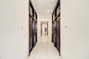 A corridor with a shiny tiled floor, flanked by dark-colored doors, leading to a bright interior space.