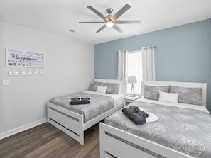 A bedroom with two beds, a ceiling fan, a wall-mounted light, a window with curtains, and a motivational quote on the wall. - Mer Sea 4 Bedroom Home (Port Bolivar)
