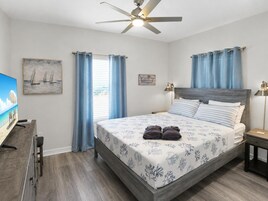 A bedroom with a bed, a ceiling fan, a TV, and a desk.