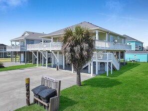 A two-story building with a covered porch and a palm tree in front. - Mer Sea 4 Bedroom Home (Port Bolivar)