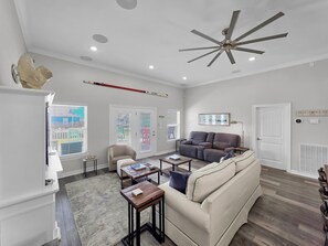 A spacious living room with a large sofa, a coffee table, and a ceiling fan. - Mer Sea 4 Bedroom Home (Port Bolivar)
