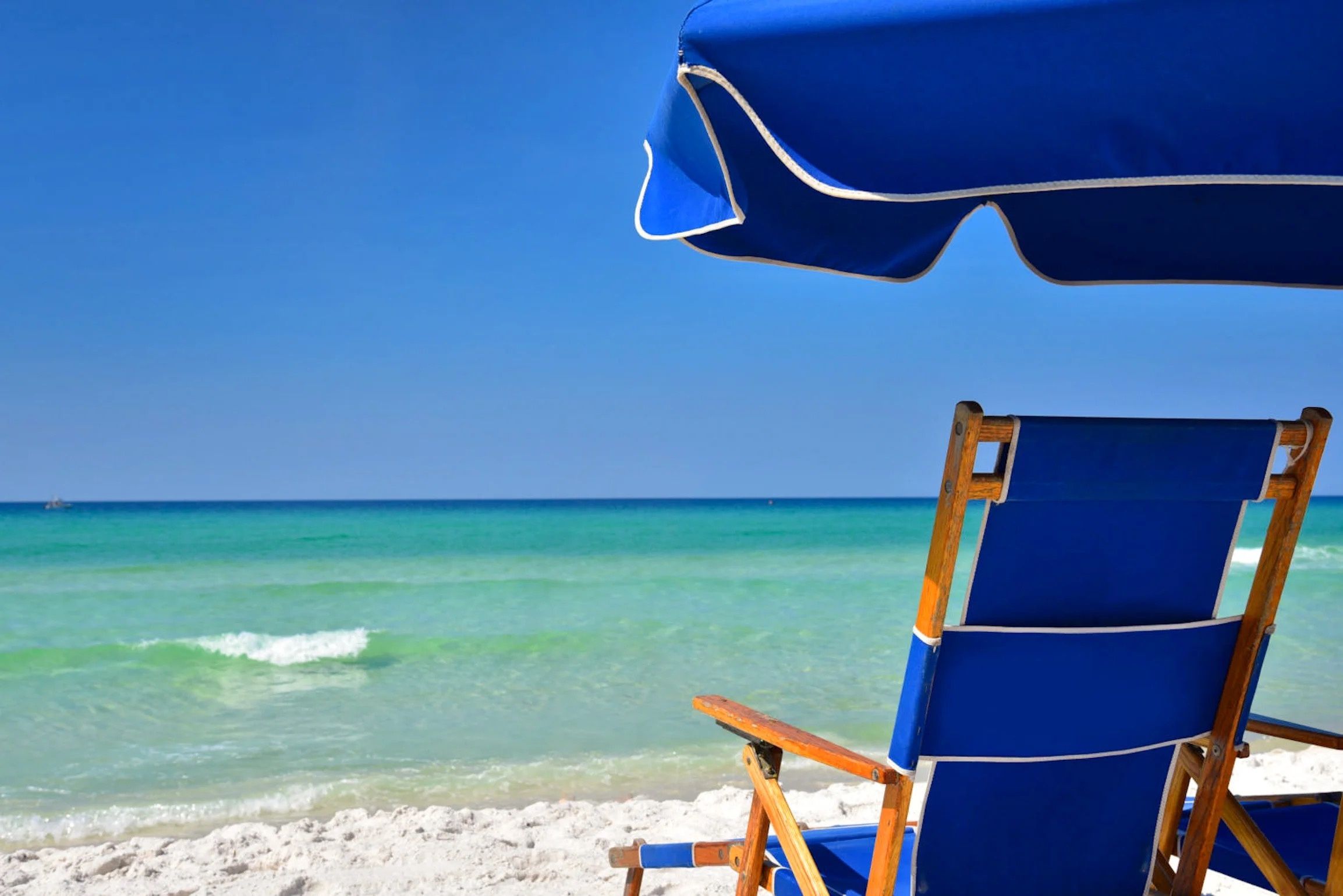 A beach chair and umbrella on a sandy beach with clear turquoise water and a clear sky.