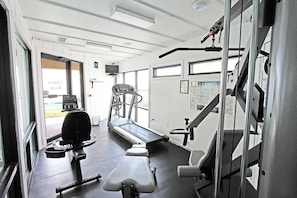 Un gimnasio con equipamiento de ejercicio, una cinta de correr y un banco de pesas.