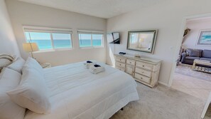 A hotel room with a large bed, a dresser, a television, and a view of the ocean. - Beach House 601a 2 Bedroom Condo (Miramar Beach)