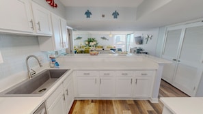 A modern kitchen with white cabinetry, a large island, and a view into the living area. - Mainsail 352 3 Bedroom Condo (Miramar Beach)