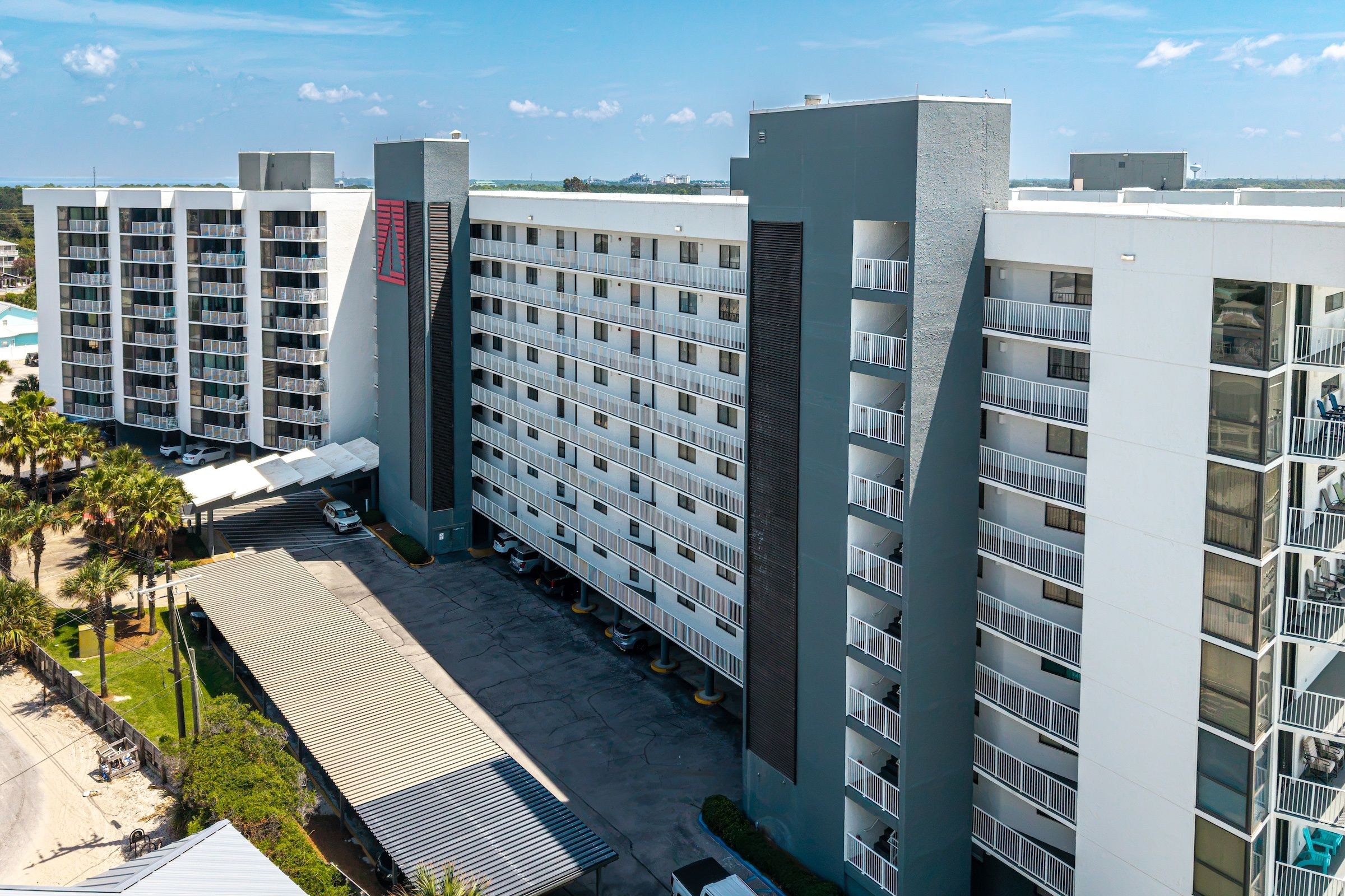Hotel com vários andares e área de estacionamento em frente, apresentando um design arquitetônico moderno com sacadas e grandes janelas.