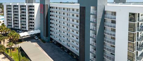 Een meerlaags hotel met een parkeerplaats ervoor, met een modern architectonisch ontwerp, балконы en grote ramen.