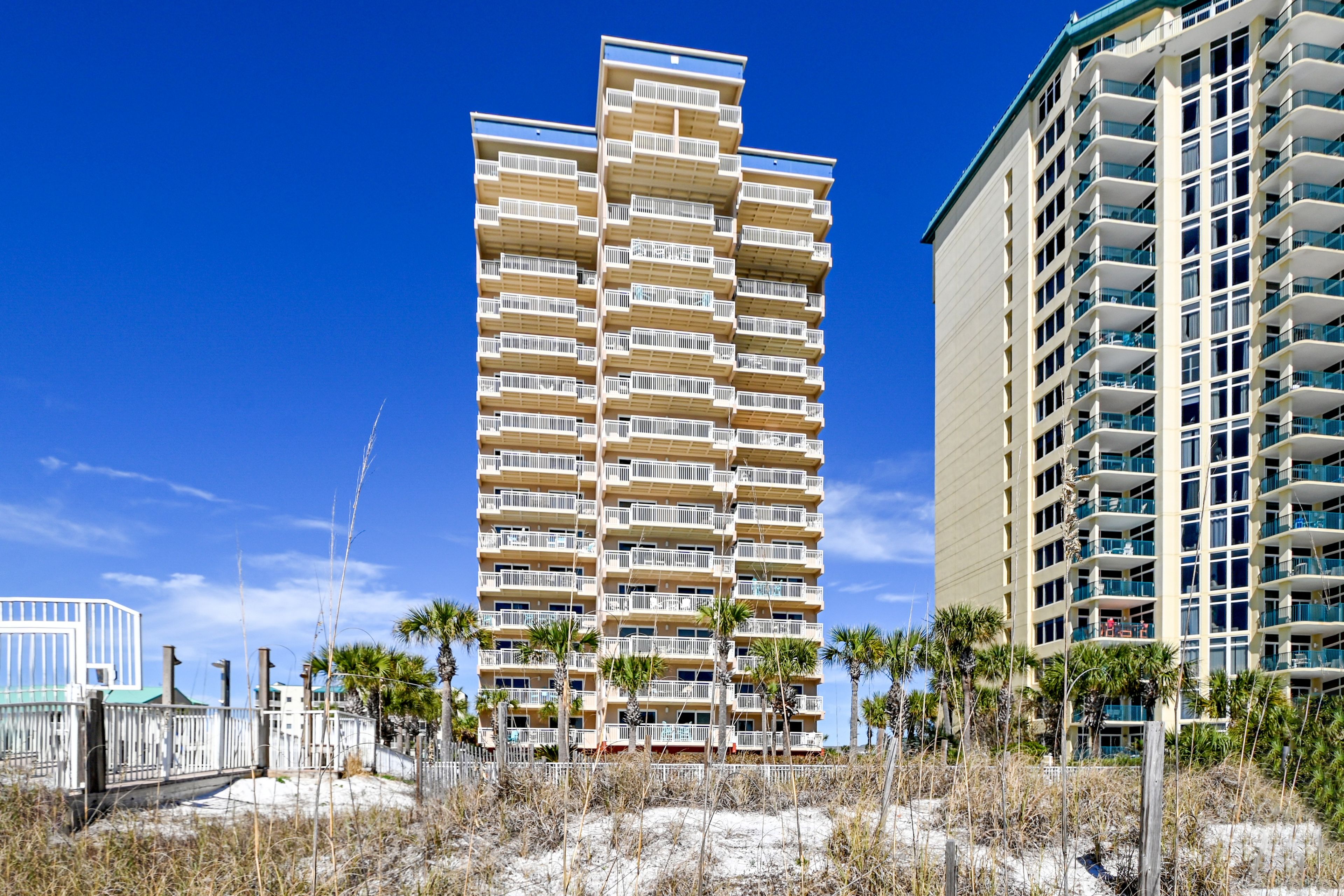 Un grand hôtel à plusieurs étages, doté de balcons, situé près d’une plage de sable.